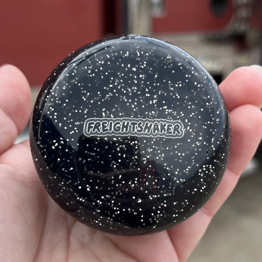 Black speckled container held in a hand with a blurred red truck in the background