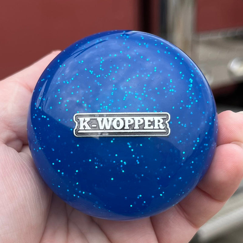 Hand holding a blue K-Wopper ball with a vintage vehicle in the background