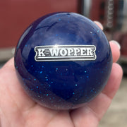 Blue knob with 'K-Wopper' logo held in a hand, blurred truck in the background