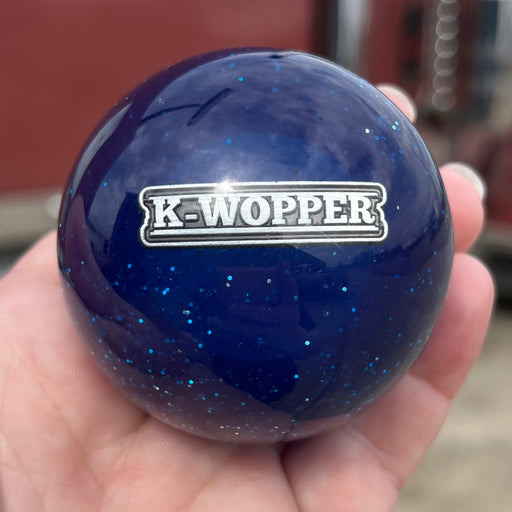 Blue knob with 'K-Wopper' logo held in a hand, blurred truck in the background