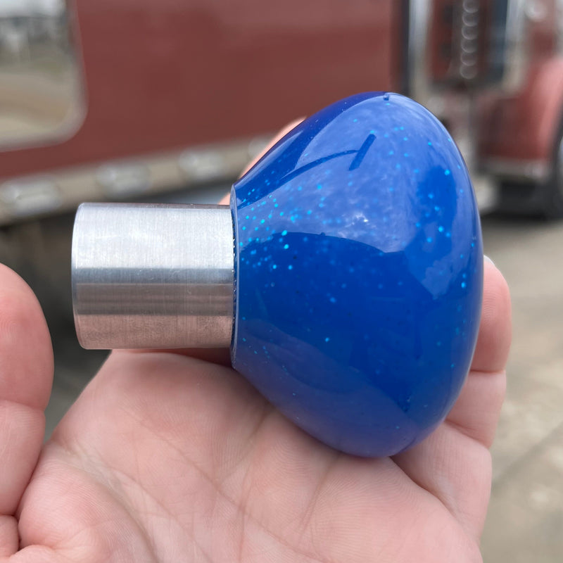 Blue knob with silver base held in a hand, with a blurred red truck in the background