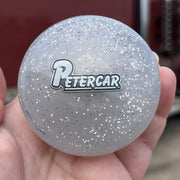 Hand holding a glittery round object with 'PETERCAR' logo in front of a truck.