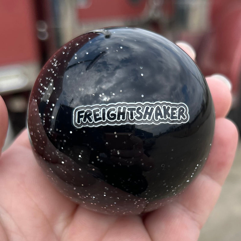 Black ball with 'Freight Shaker' logo held in a hand, blurred truck in the background