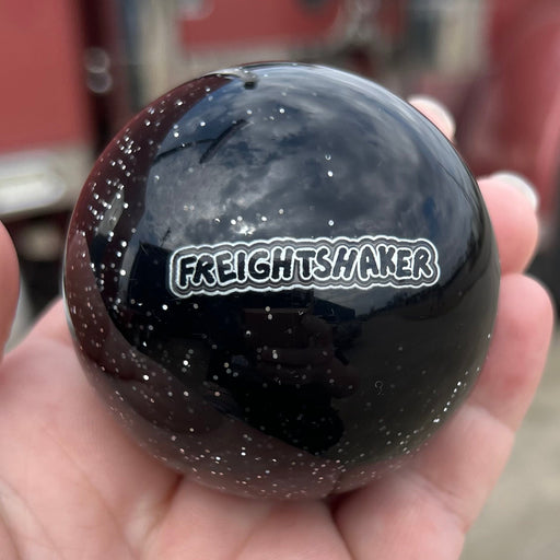 Black ball with 'Freight Shaker' logo held in a hand, blurred truck in the background