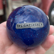 Blue glittery ball with 'Freightliner' branding held in a hand, with a blurred truck in the background.