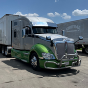 Green and silver truck with a trailer in a parking lot under a blue sky.