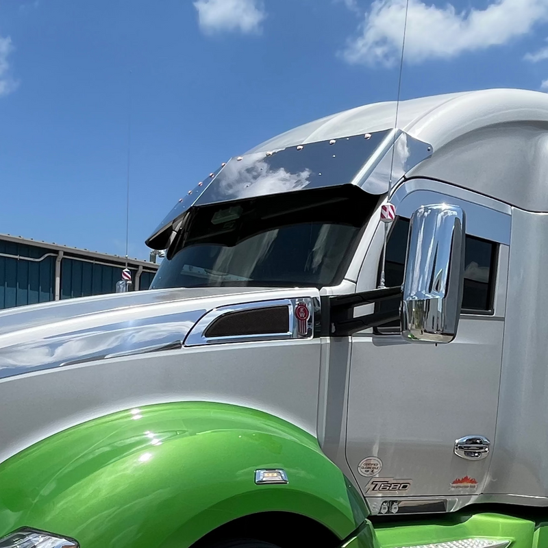 Green and silver semi-truck parked on a concrete surface with a blue sky in the background.