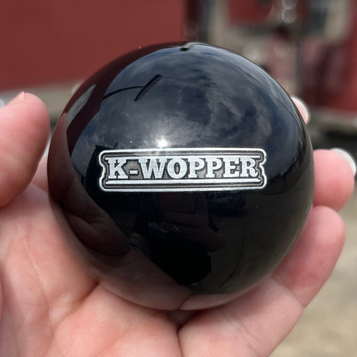 Black knob with 'K-Wopper' logo held in a hand, with a red truck in the background.