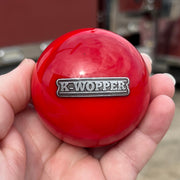 Red ball with 'K-Wopper' logo held in a hand, blurred red truck in the background