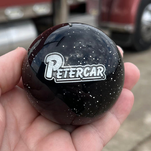 Hand holding a black object with 'PETERCAR' logo in front of a red truck.