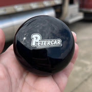 Black knob with 'Petercar' logo held in a hand, with a truck in the background