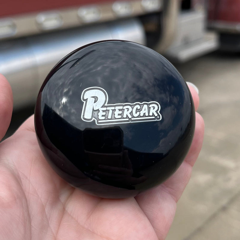 Black knob with 'Petercar' logo held in a hand, with a truck in the background