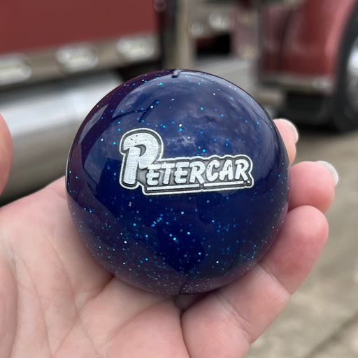 Hand holding a blue ball with 'Petercar' logo in front of a red truck.