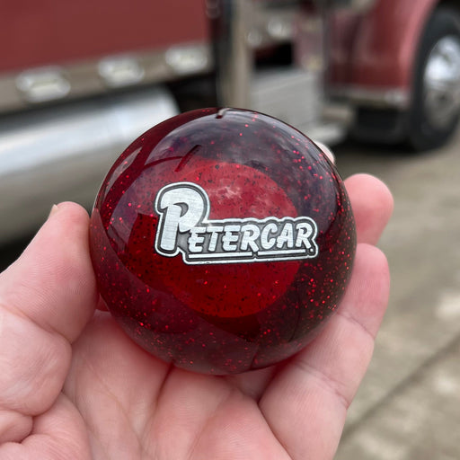 Red round object with 'PETERCAR' logo held in front of a large red truck.