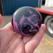 Hand holding a marbled black and pink object with a blurred background