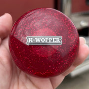 Red glittery knob with 'K-Wopper' logo held in a hand, blurred truck in the background