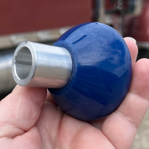 Hand holding a blue and silver metal fitting with a truck in the background