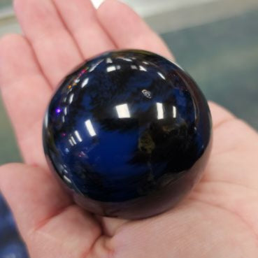 A hand holding a round, marbleized blue and black gear shift knob with a adapter.